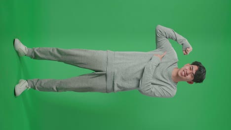 full body of smiling asian man pointing bicep while standing in front of green screen background
