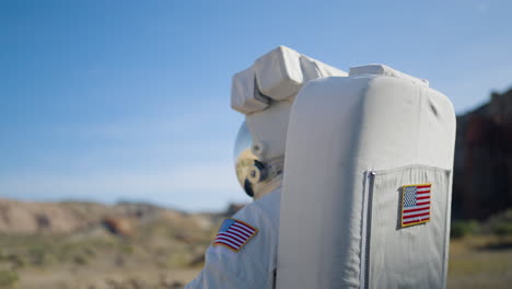 Astronaut-looking-around-deserted-terrain,-equipped-with-a-mirroring-visor-and-space-gear