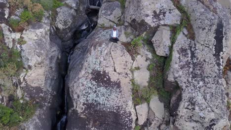 A-man-meditating-on-the-rocky-cliff-of-a-mountain-in-Madeira,-Portugal---Aerial-shot