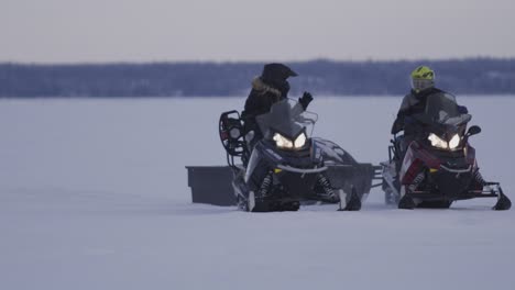 2 snowmobiles driving and stopping on a frozen lake