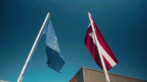 the flags of the european union and the republic of latvia flutter side by side under a bright blue sky on a sunny day