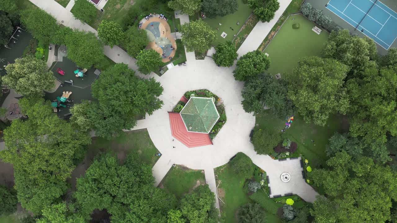 360 aerial rotation around Liberty State Park gazebo in Jersey City. Symmetrical park layout with trees, paths, and skyline glimpses