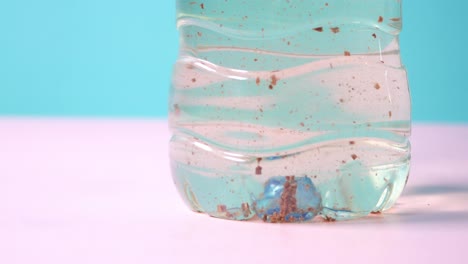 a close-up of a plastic water bottle with sediment and a blue marble at the bottom