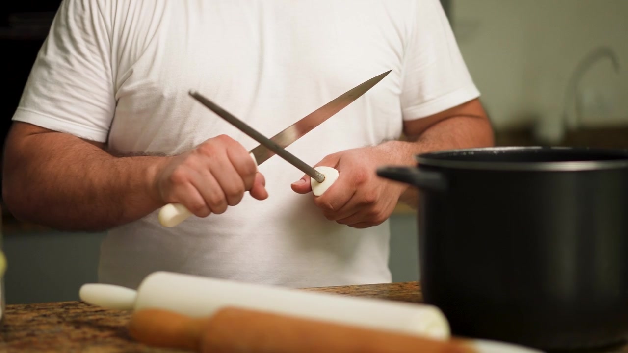 Primo piano di uno chef che affila un coltello, preparandosi per la preparazione dei pasti