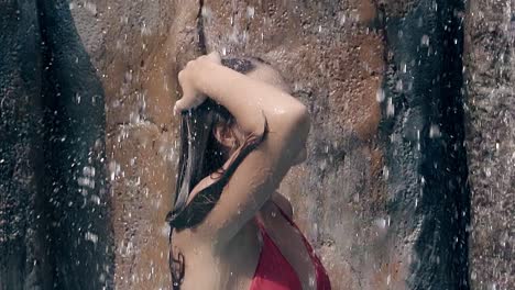 slim woman with long hair relaxes under artificial waterfall