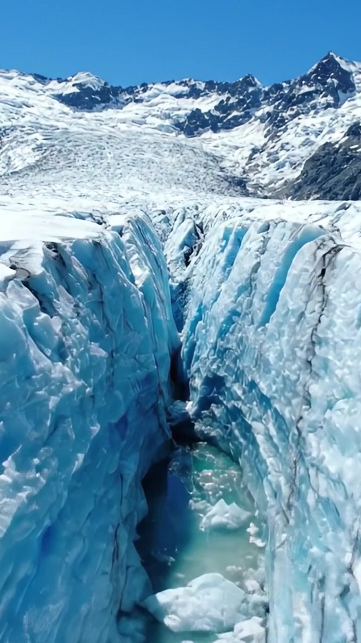 Impresionante grieta glacial rodeada de imponentes formaciones de hielo y majestuosos picos montañosos bajo un cielo azul brillante