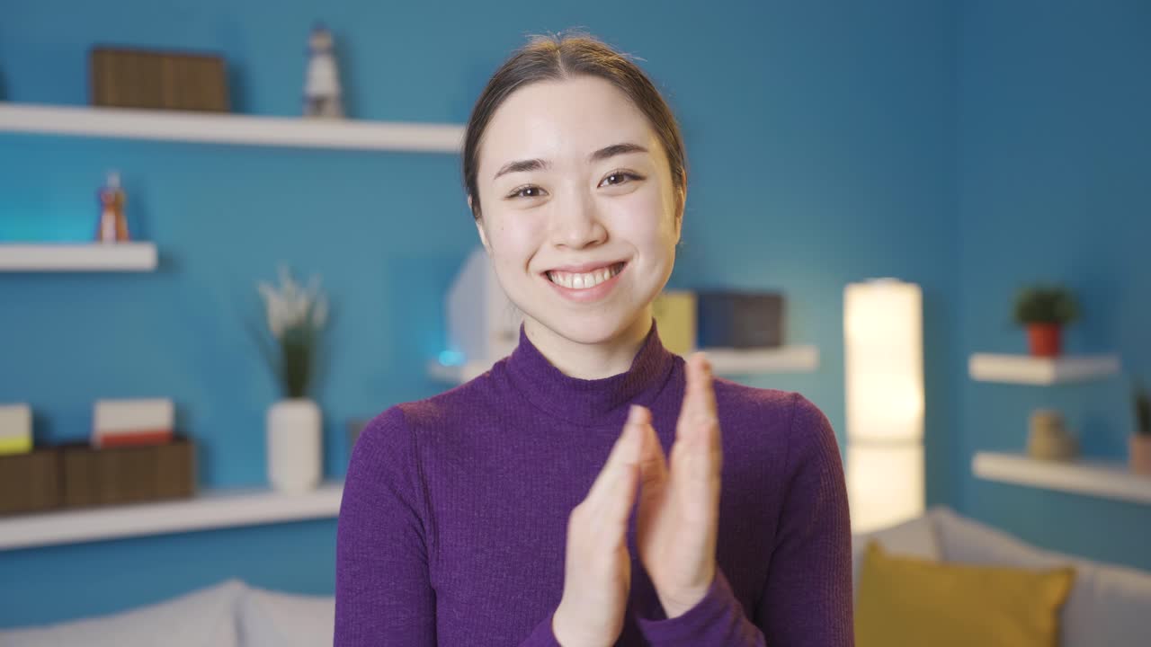 아시아 여성이 카메라를 쳐다보며 행복하게 박수를 치고 있습니다.