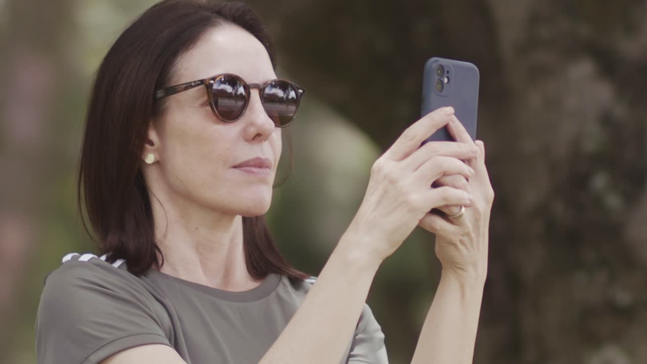 Brunette woman wearing sunglasses, panning smartphone media capture