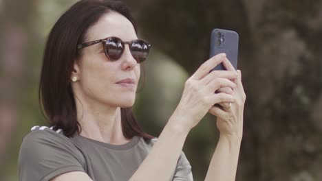 brunette woman wearing sunglasses, panning smartphone media capture