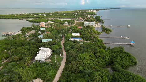 drone view in belize flying over caribbean sea, a caye covered with palm trees and restaurants on a cloudy day