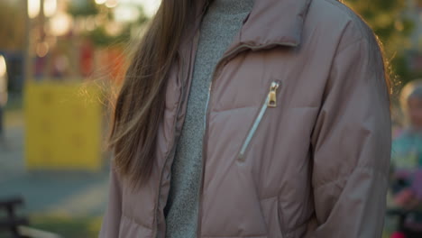 un primer plano de una chica sonriente con una chaqueta de melocotón y de pie en patines en un parque. el fondo está suavemente borroso, expresión feliz y la luz suave que se refleja en su cabello