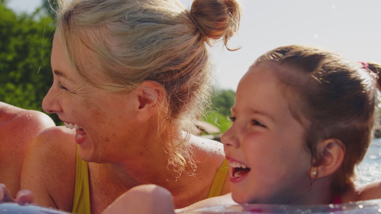Lächelnde Mehrgenerationenfamilie entspannt sich im Sommerurlaub auf einer Luftmatratze im Schwimmbad.