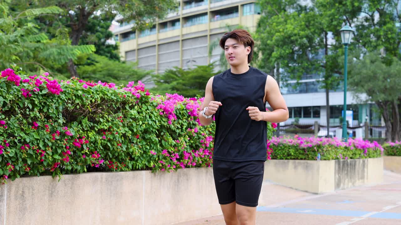 Seorang pria Asia yang sedang jogging melewati hamparan bunga berwarna-warni di taman kota yang cerah, gerakan kamera stabil