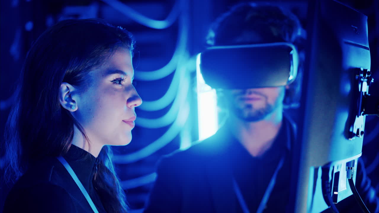 Woman programming in a server room while a man is using a Virtual Reality headset