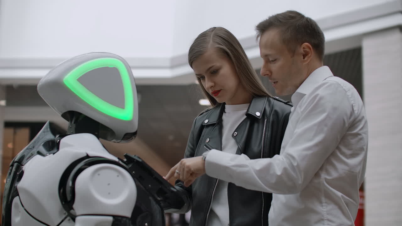 dos personas un hombre y una mujer se comunican con un robot. presiona el robot con las manos en la pantalla. un asistente robot interactuando en un centro comercial con una pareja. asistente robot en el piso de negociación