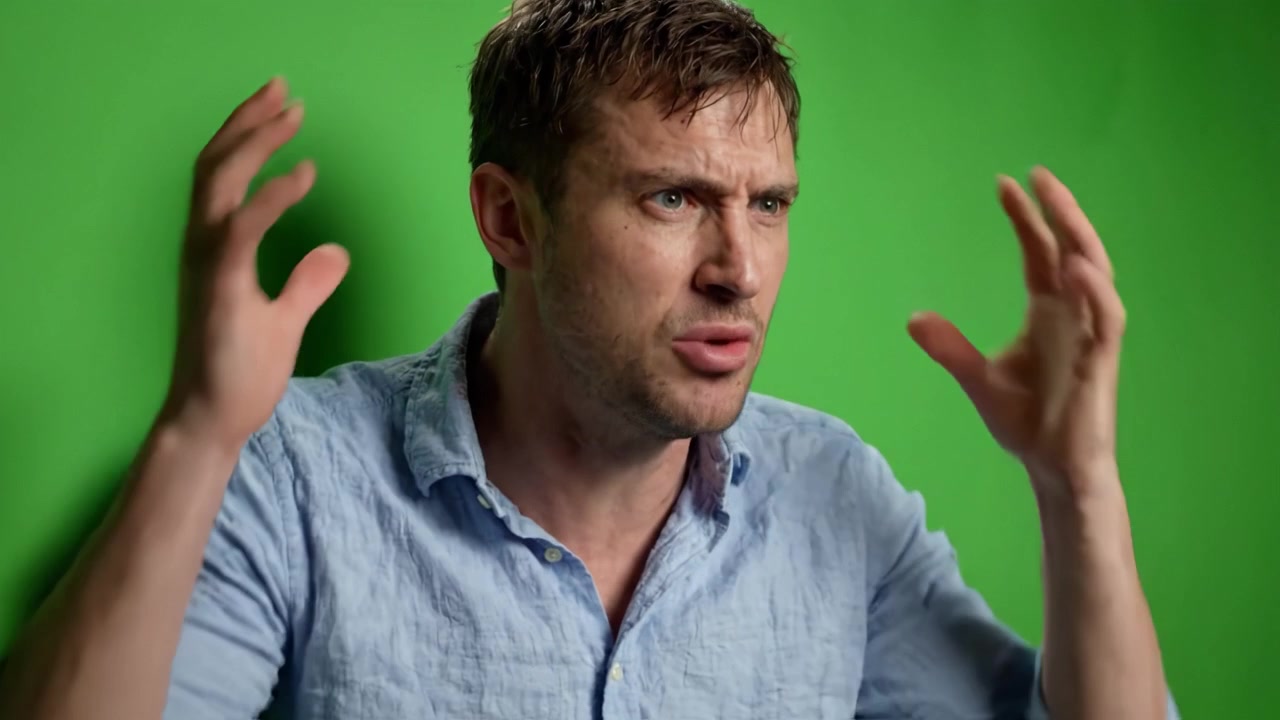 A man in distress expresses strong emotions while sitting against a green backdrop, showcasing deep feelings of frustration and overwhelm as he covers his face with his hands.