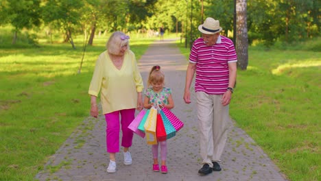 child girl kid walking with senior retired grandmother grandfather with colorful bags after shopping