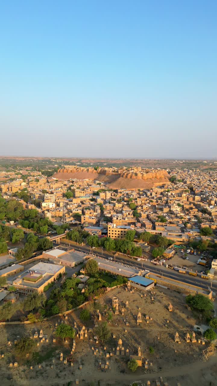A stunning 4K drone view captures the majestic Jaisalmer Fort, also known as the Golden Fort, towering over the historic Rajasthan cityscape on a bright, sunny day in India