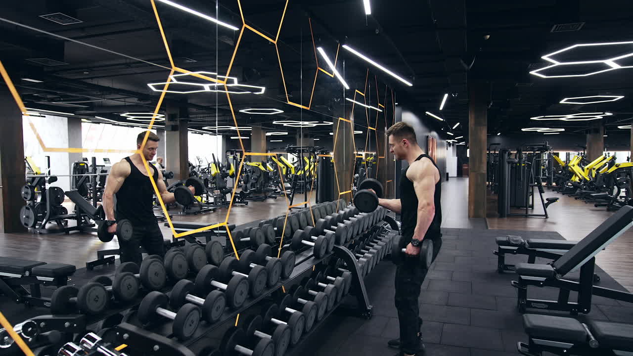Iniciando ejercicio con pesas mancuernas. Joven en forma con ropa deportiva concentrado en levantar mancuernas mientras se ejercita en el gimnasio