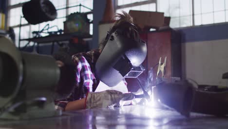 female mechanic wearing welding helmet welding while sitting at car service station