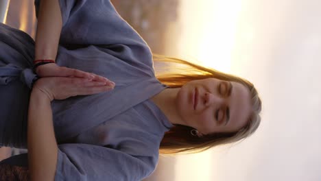 peaceful blonde woman standing on terrace with closed eyes, namaste gesture