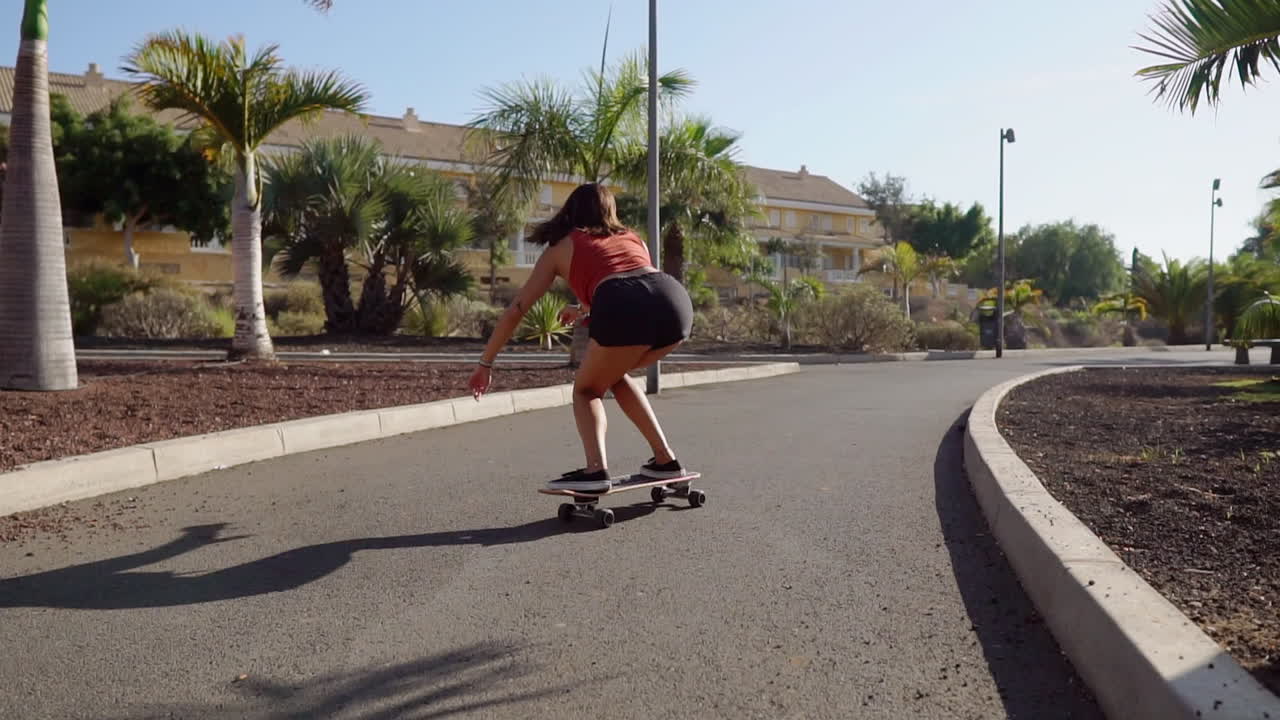 A young girl's leisurely ride on her longboard along the beach road is beautifully depicted in slow motion against the backdrop of palm trees