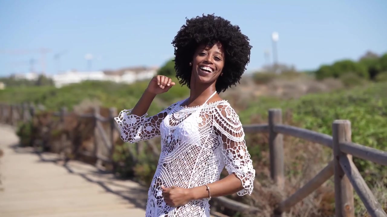 Donna afroamericana con capelli afro che balla su un sentiero di legno vicino alla spiaggia