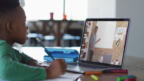niño afroamericano haciendo la tarea mientras tiene una videollamada con un profesor masculino en una computadora portátil en casa