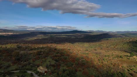 flight-in-reverse-in-an-agricultural-area-with-trees-in-autumn-with-mountains-in-the-background-a-blue-sky-with-clouds-we-see-agricultural-fields-and-a-house-in-ruins-on-a-road-and-cars-driving