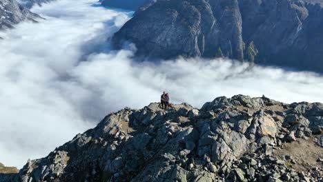 drone orbits a couple standing at the edge of bakkanosi cliffs, revealing the distant fjord below filled with fog