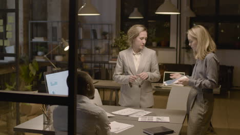 female employee is showing graphics on the tablet to an american male coworker and female coworker in the office