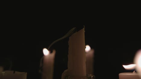 An-extreme-close-up-of-white-candles-lit-with-a-black-background-one-gets-blown-out