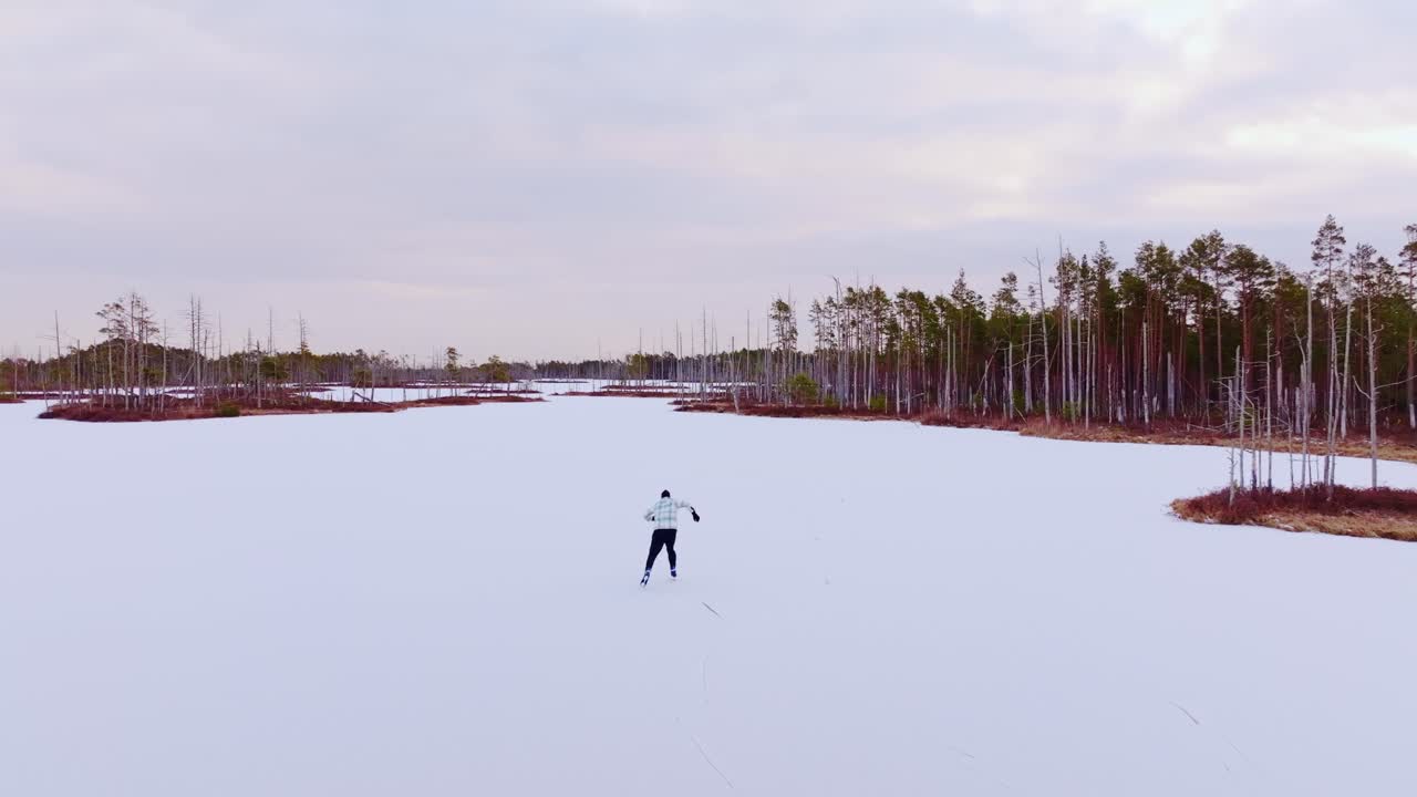 Zeitlupe aus der Rückansicht eines Mannes, der im Winter auf einem schneebedeckten Moorsee Schlittschuh läuft