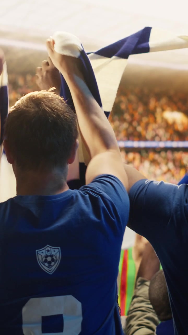 Video verticale. Primo piano di tifosi di calcio felici che sollevano le sciarpe in uno stadio affollato.