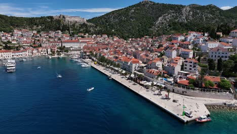 Establishing drone shot of Hvar harbor during the day with Adriatic Sea, boats and castle in Croatia, orbit drone shot