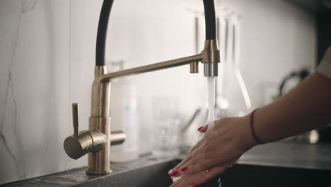 housewife is washing hands in kitchen woman is opening tap closeup view if female hands