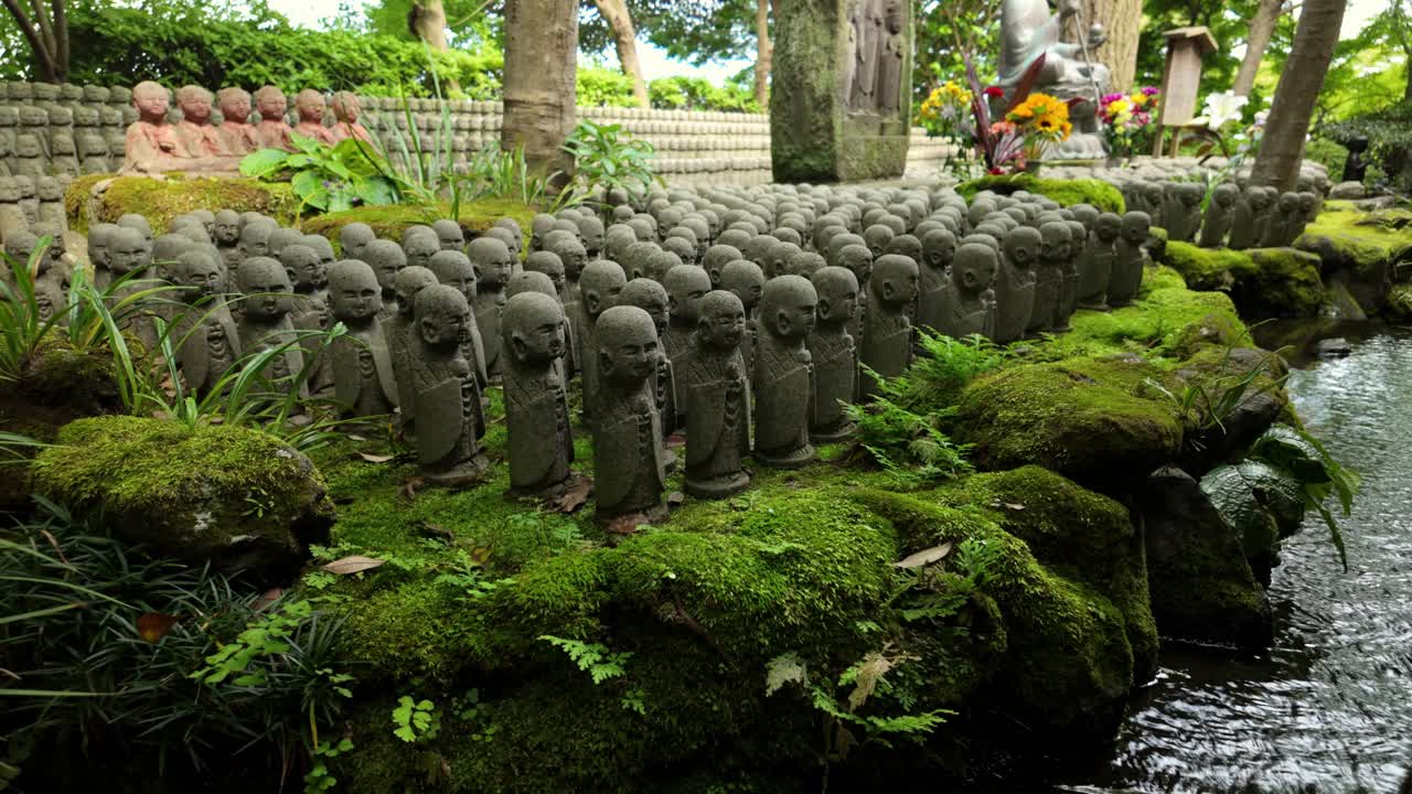 Static shot of hundreds of small stone Jizo statues lined along a moss-covered pond in a peaceful temple garden at Hasedera in Kamakura, Japan
