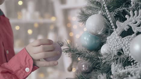 un niño curioso recoge la decoración rosa del árbol de navidad.