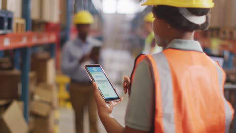 African-american-female-worker-with-helmet-using-smartphone-in-warehouse