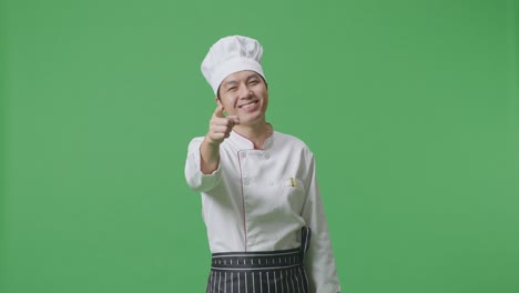 chef asiático sonriendo y tocando su pecho luego señalándote mientras está de pie en el estudio de fondo de la pantalla verde