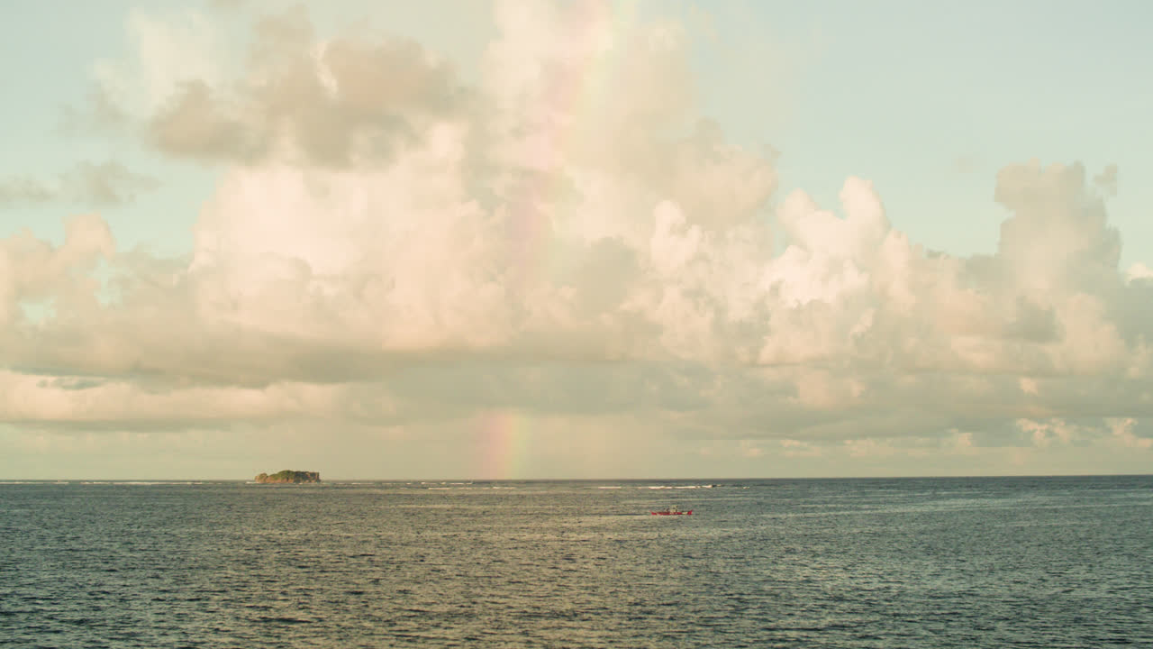A view from Siargao of a boat sailing by a rainbow and calm waters of the Pacific Ocean.