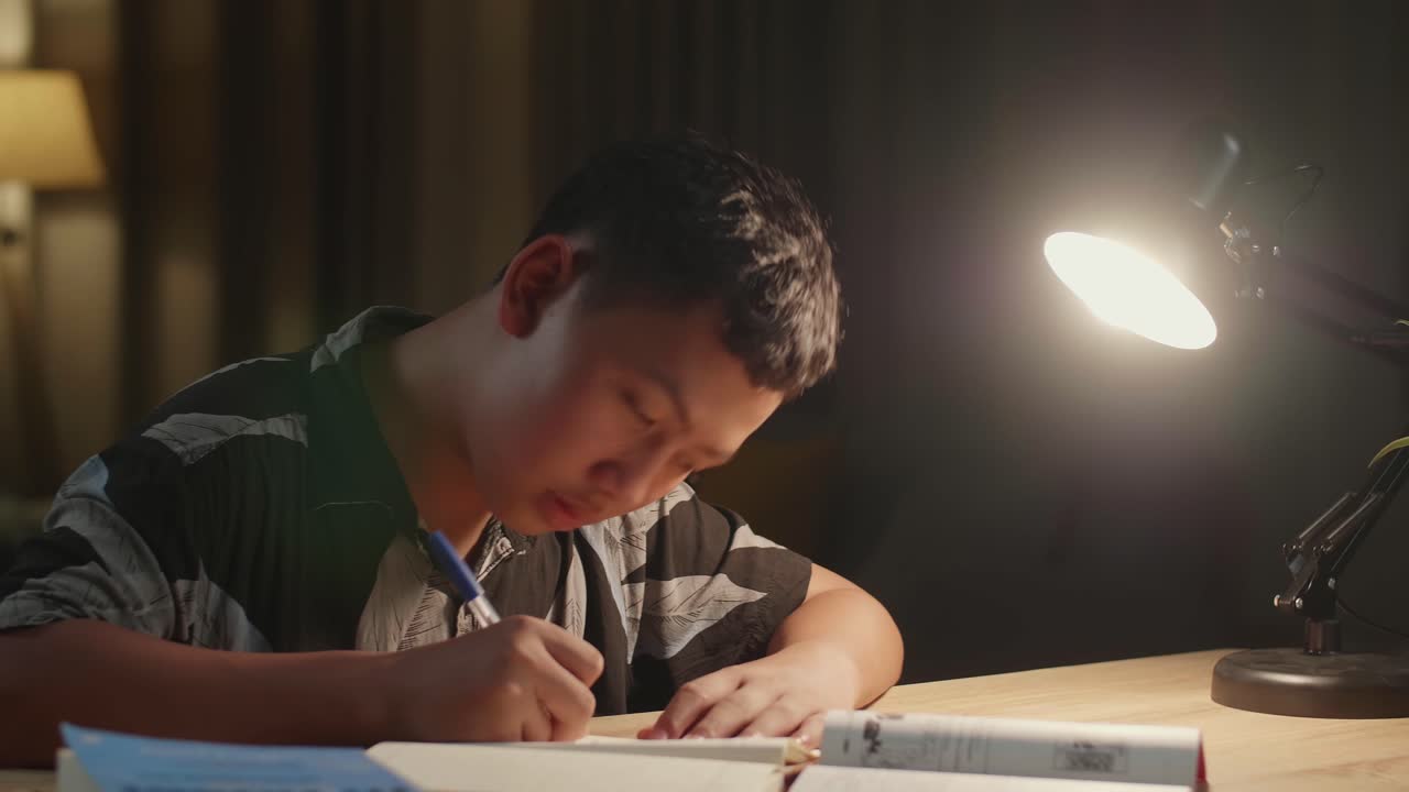 Asian Boy Is Studying At Home, Asia Child Writing While Sitting On The Table At Night