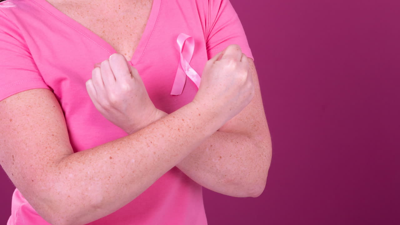 Video of midsection of caucasian woman with crossed arms wearing pink cancer awareness ribbon
