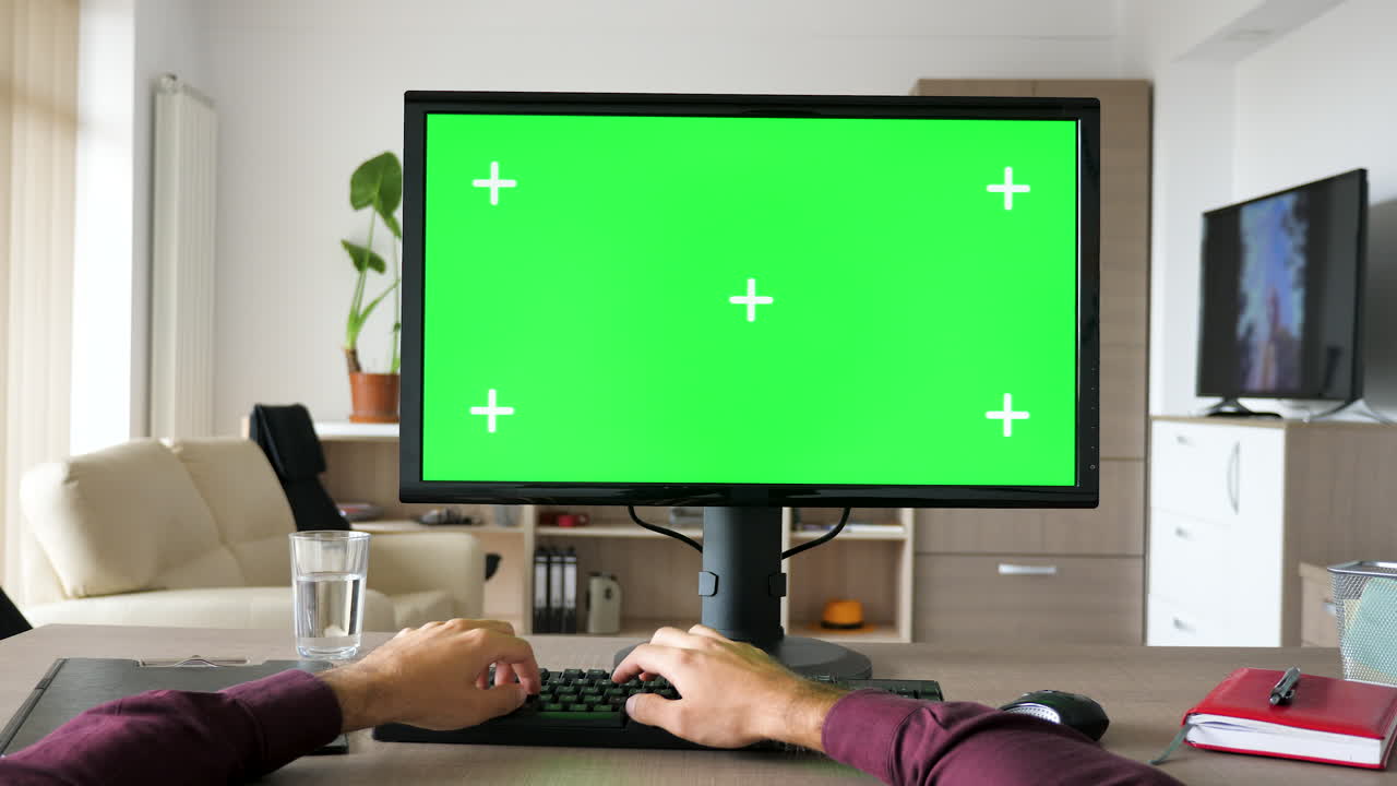 Person working at a desk with a computer with a green screen