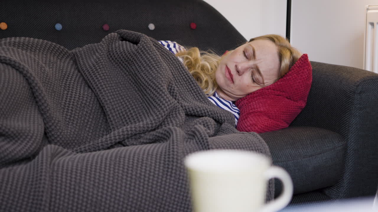 Donna che dorme sul divano con coperta e cuscino
