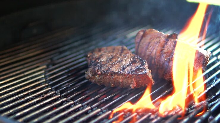 Turning tender beef steaks being grilled on the barbecue flames - slow motion