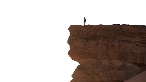 hombre caminando sobre un acantilado empinado de arenisca en un desierto con luz solar en la parte posterior de la vista amplia