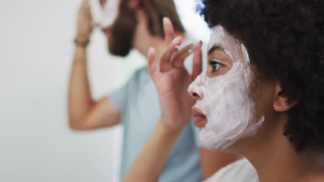 pareja de raza mixta aplicando una máscara facial juntos en el baño
