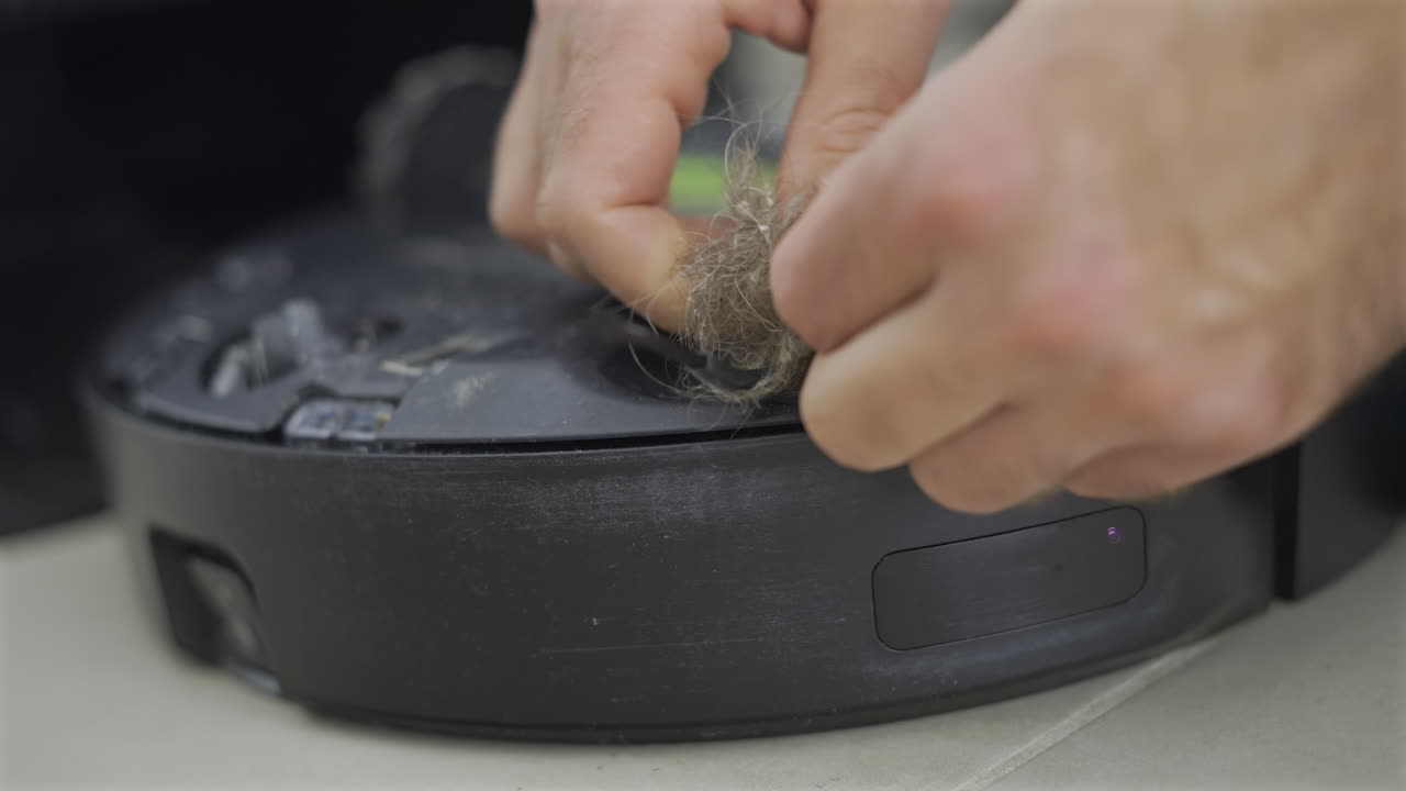 Close up of a man's hand cleaning the back of a robot vacuum cleaner