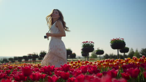 beautiful girl with camera walking through tulip field. woman smiling in garden.